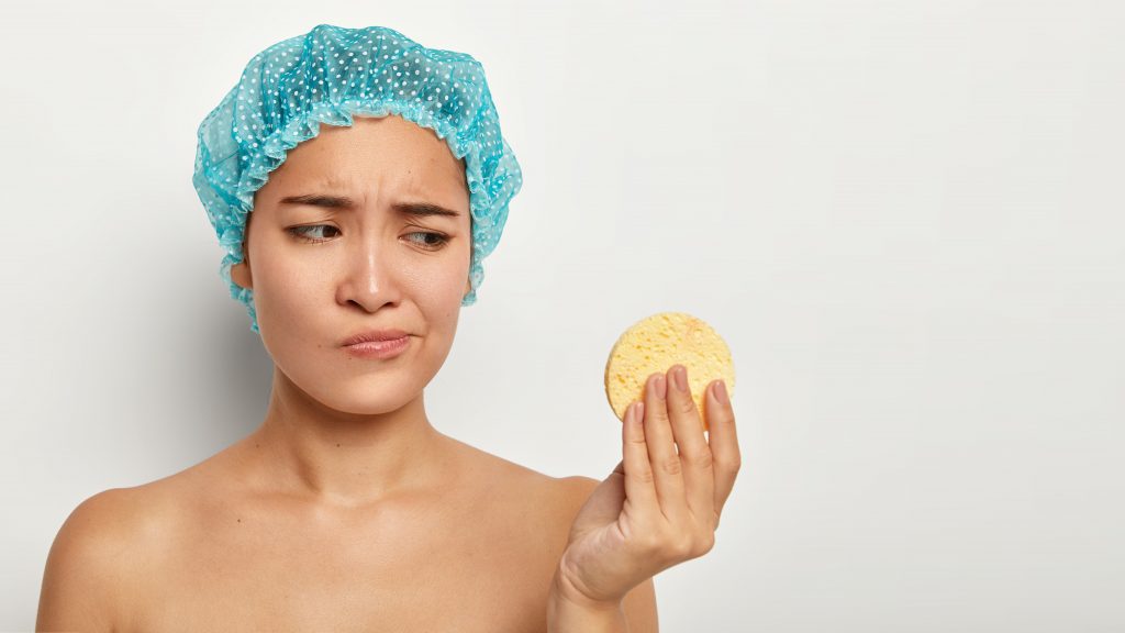 youth-pampering-cleaning-and-skin-care-concept-dissatisfied-young-chinese-woman-looks-unhappily-at-cosmetic-sponge-removes-face-makeup-wears-blue-protective-headgear-isolated-on-white-wall-2